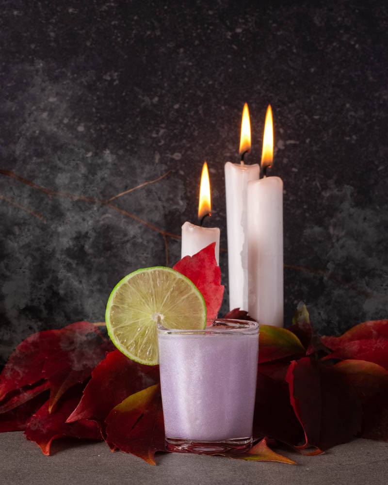 Der fertige Drink unseres Rezept "Glitzer Spritzer" angerichtet mit einem Limettenschlitz und Kerzen für die perfekte Halloween Stimmung.