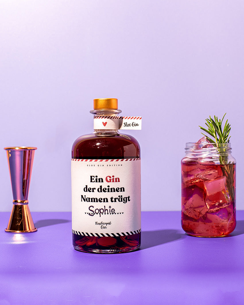 "Ein Gin der deinen Namen" ist der Spruch auf dem Etikett unserer Sloe Gin Edition mit Schlehenbeeren, er steht neben einem Jigger und einem leckerem Drink.