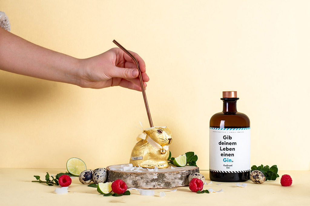 Ein Strohhalm wird in den Schokoladenhasen gesteckt, sodass man den perfekten Oster Drink mit Flaschenpost Gin aus dem Schokoladen Hasen genießen kann