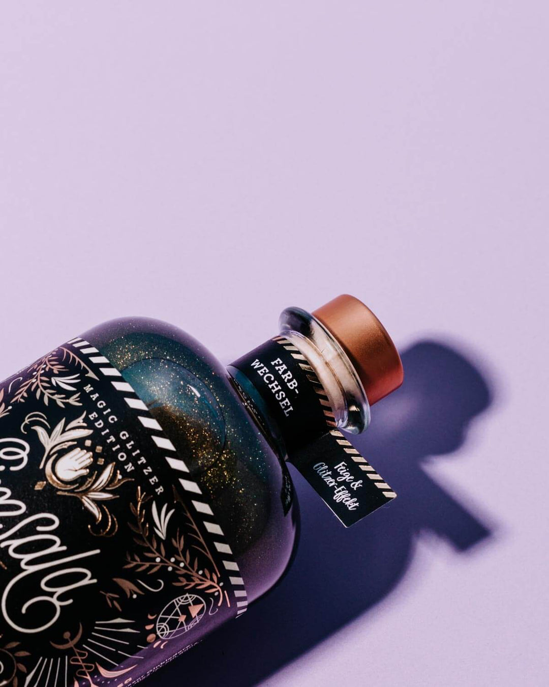 Das gold schwarze Etikett unseres glitzernden Simsala Gins mit Farbwechsel und dem Fähnchen am Flaschenhals auf dem das Botanical "Feige" und "Farbwechsel" steht.