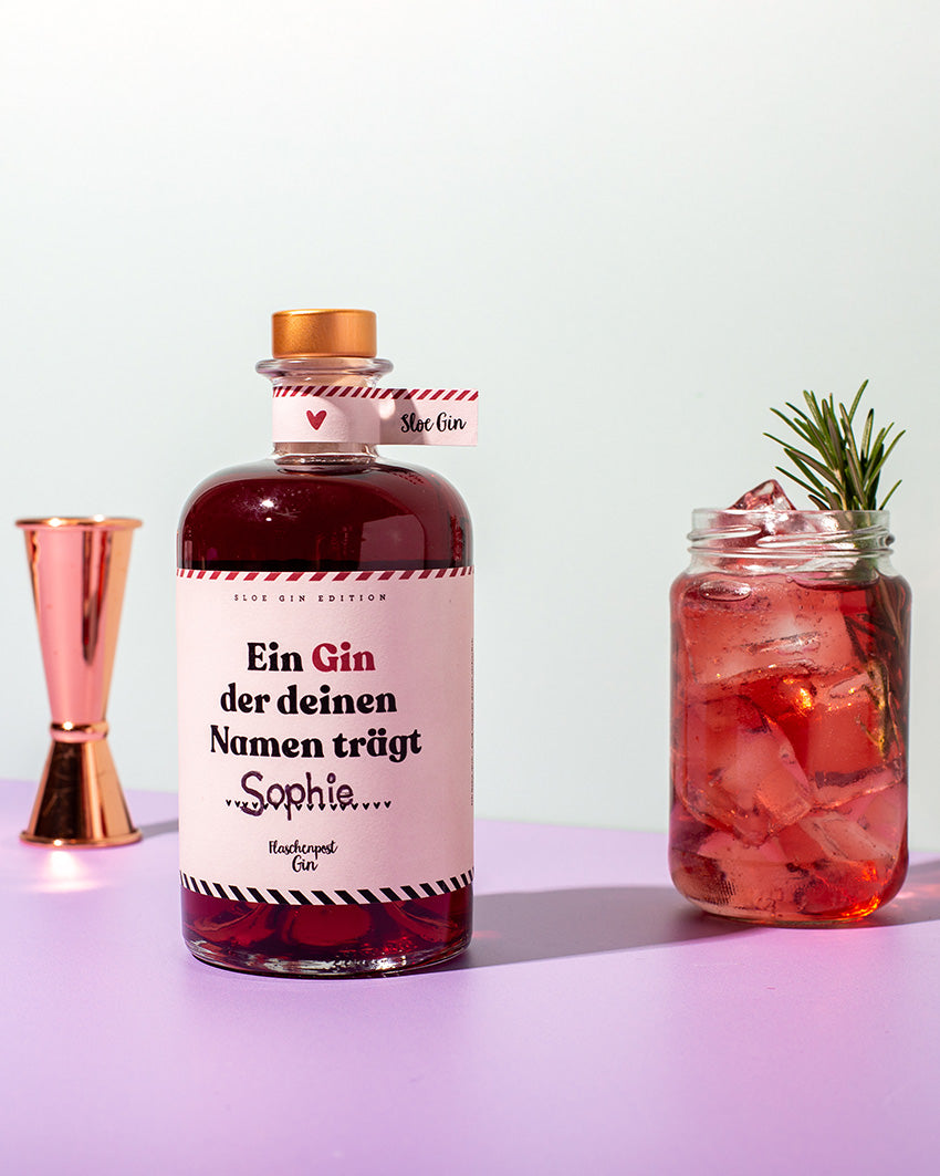Auf dem Etikett unserer Sloe Gin Edition mit Schlehenbeeren steht der Slogan "Ein Gin, der deinen Namen trägt", im Hintergrund ein Jigger und ein köstliches Getränk.