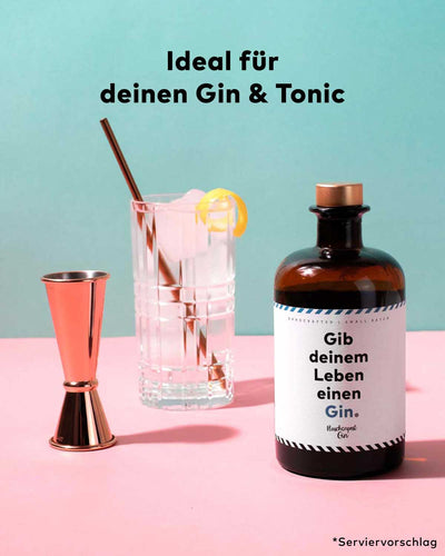 "Gib deinem Leben einen Gin" von Flaschenpost, daneben ein Jigger und ein Gin Tonic im Highball Glas. 